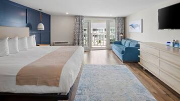 Ett modernt hotellrum med en stor säng, en blå soffa, en TV och en balkong med utsikt.