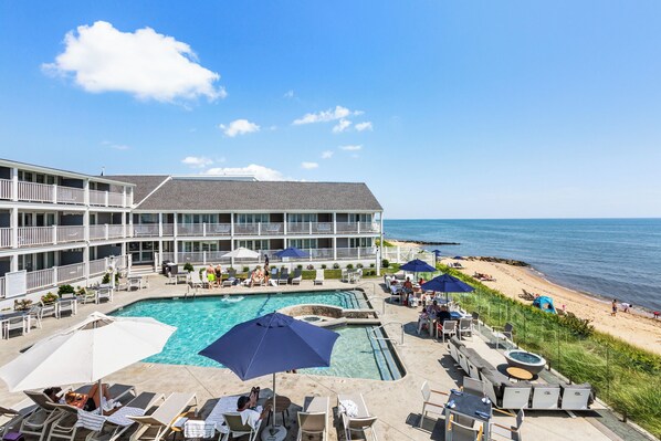A hotel with a pool, lounge chairs, umbrellas, and a beach view. - Pelham House Resort (Dennis Port)