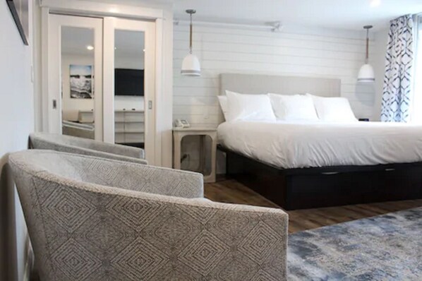 A bedroom with a large bed, a bedside table, a nightstand, and a chair.