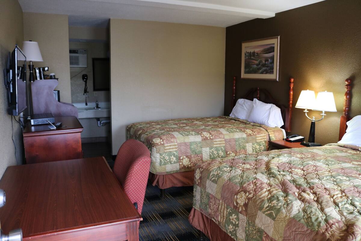 A hotel room with two beds, a desk, a chair, a desk lamp, a telephone, and a painting on the wall.