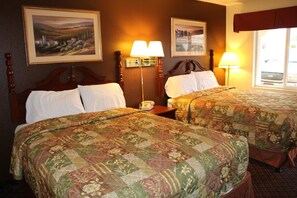 Habitación de hotel con dos camas, cada una con ropa de cama estampada con motivos florales, cabeceros de madera, una lámpara de noche y una mesita con teléfono.