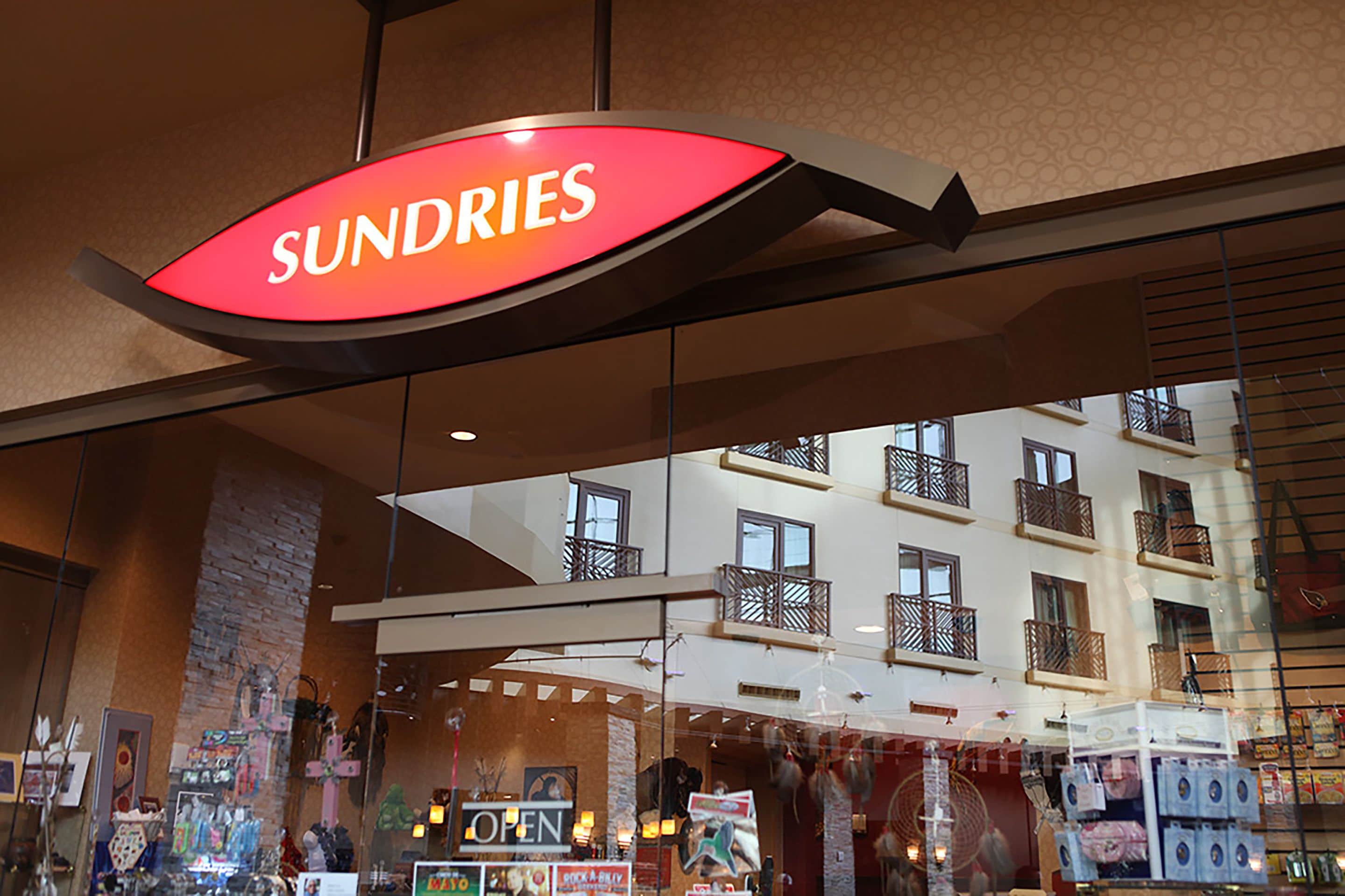 A hotel interior with a visible sign reading "SUNDRIES" and a reflection of a building with balconies.