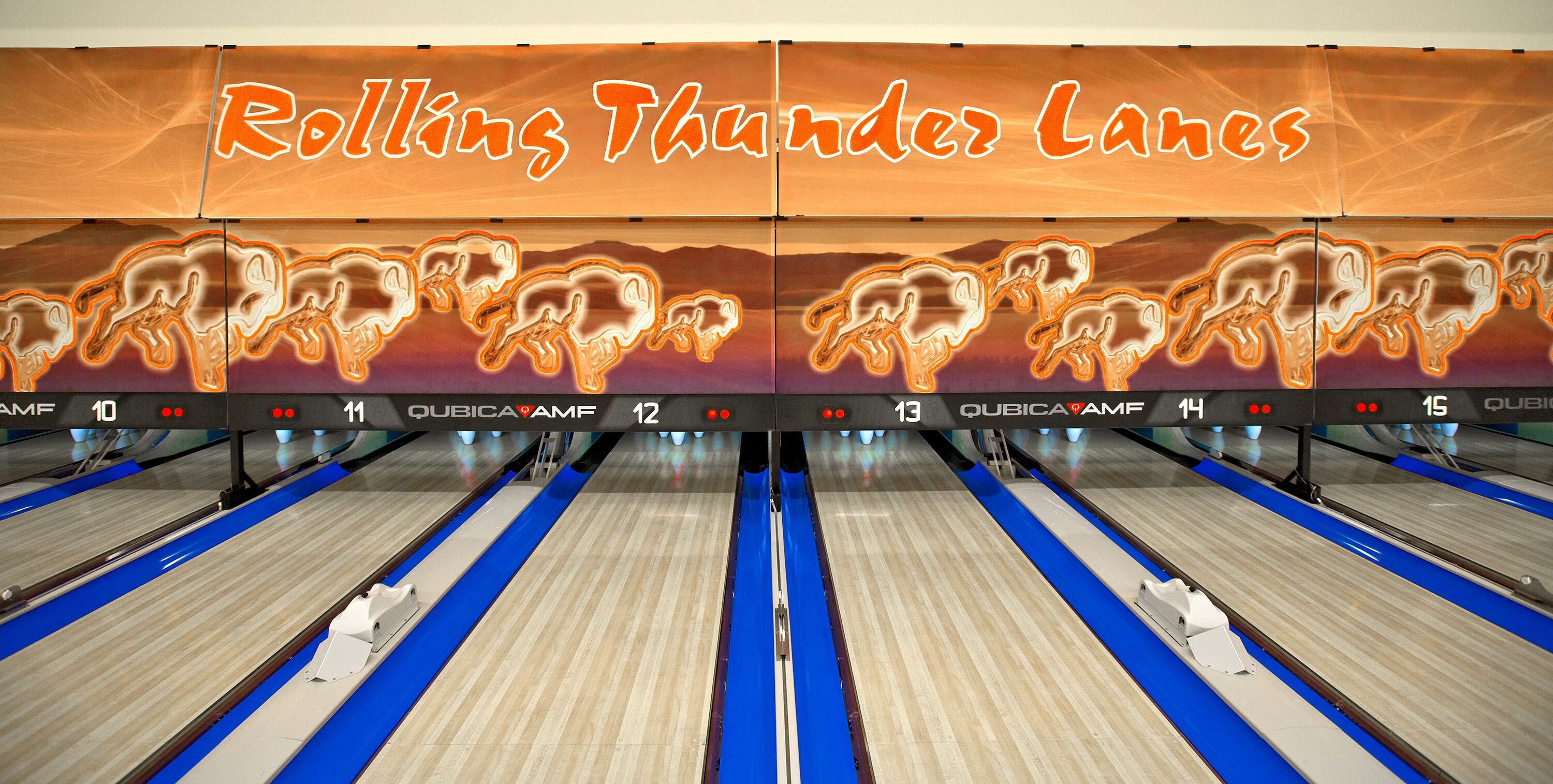 Una bolera con pistas numeradas del 10 al 15, un letrero de neón que dice 'Rolling Thunder Lanes' y el nombre de la marca 'QUBICA AMF' en las pistas.