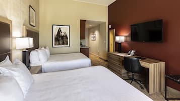 Een hotelkamer met twee bedden, een bureau, een stoel, een televisie en kunstwerken aan de muur.