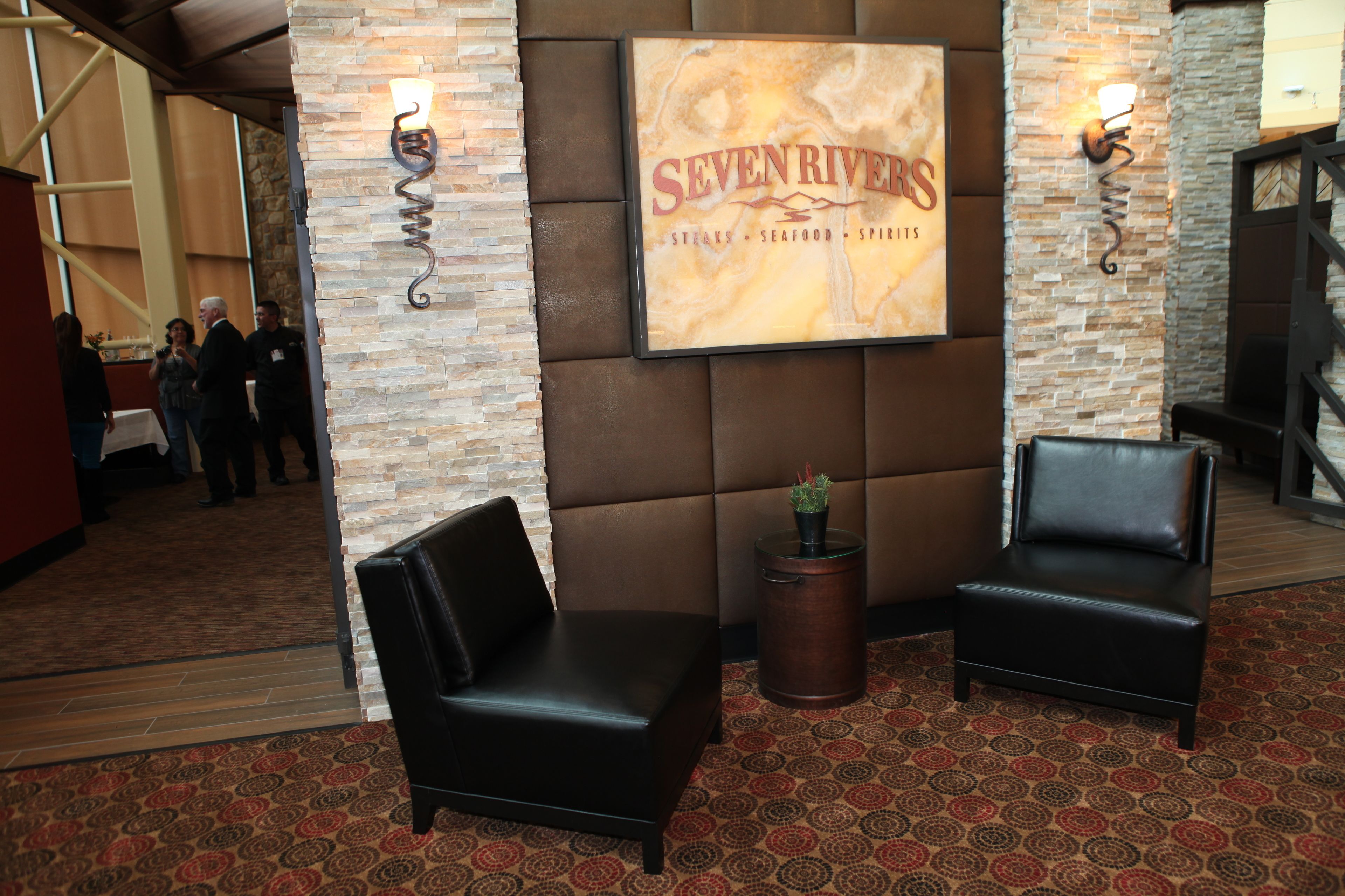 A lobby with a stone wall, a sign reading "SEVEN RIVERS," two black leather chairs, and a patterned carpet.