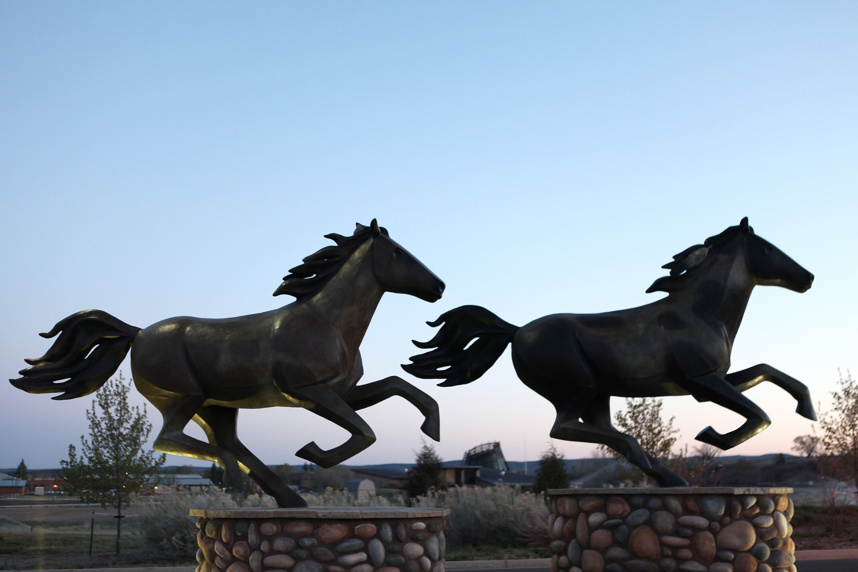 Two bronze horse statues on pedestals in an outdoor setting.