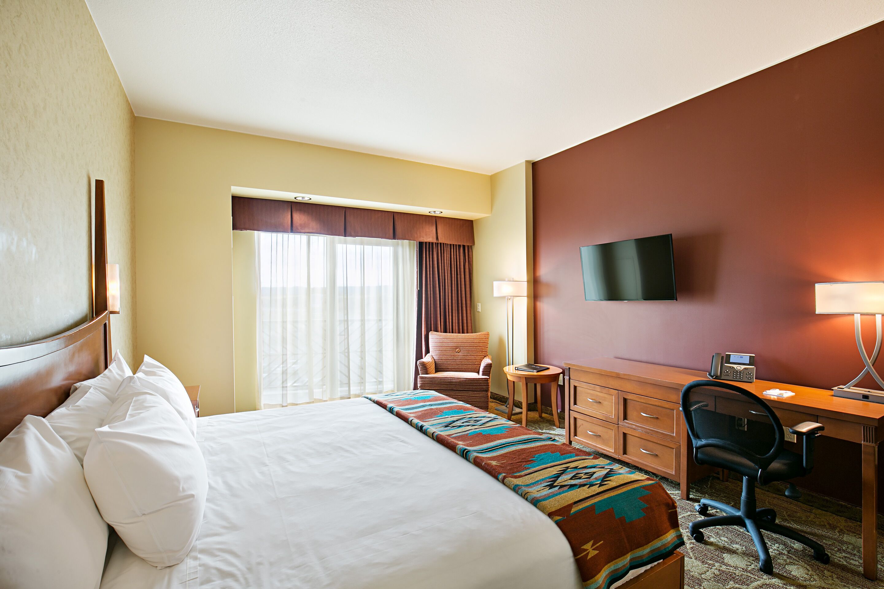 A hotel room with a bed, a desk, a chair, a television, and a window with curtains.