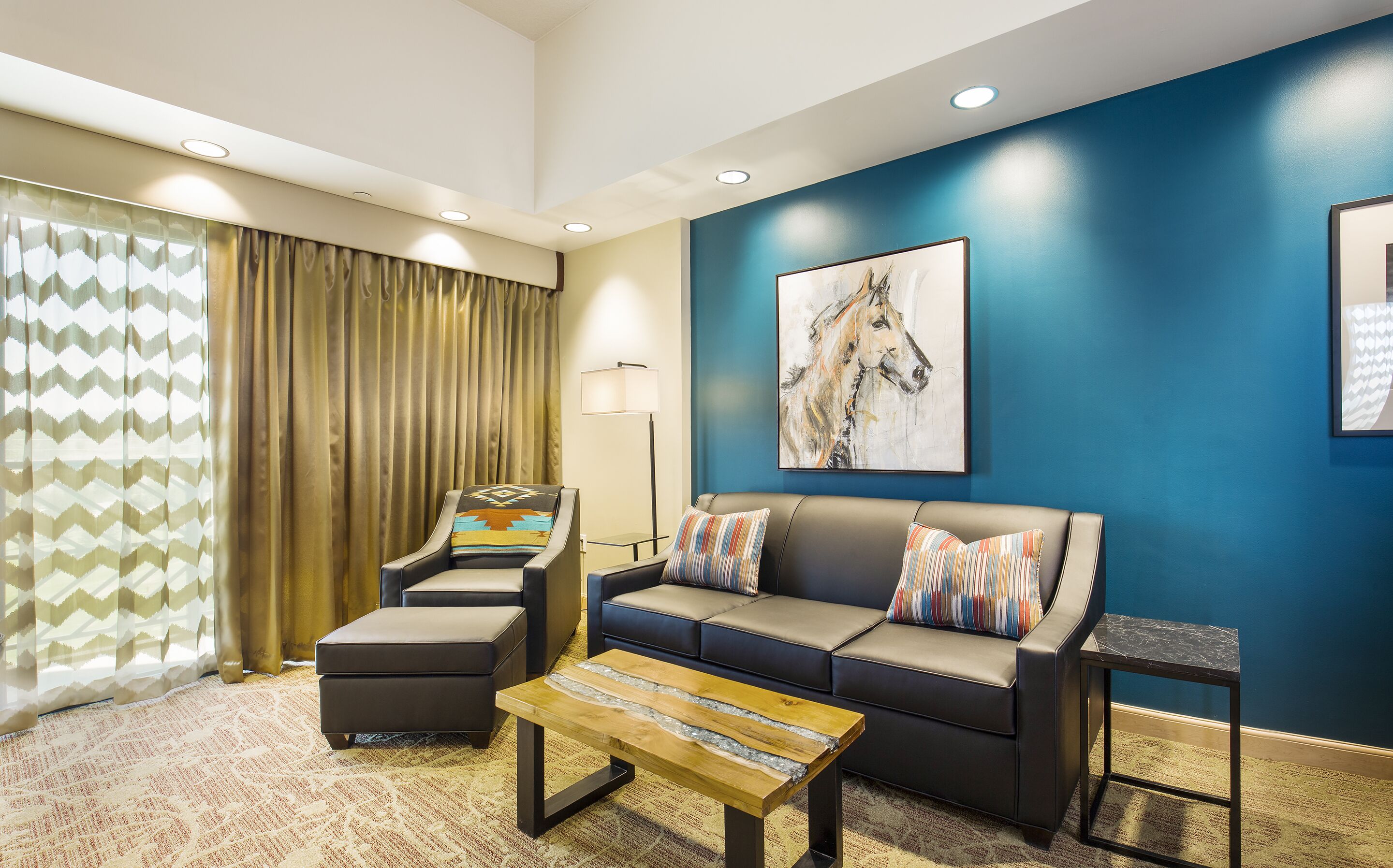 A modern living room with a blue accent wall, a sofa with striped pillows, a coffee table, and a chair with a patterned throw.