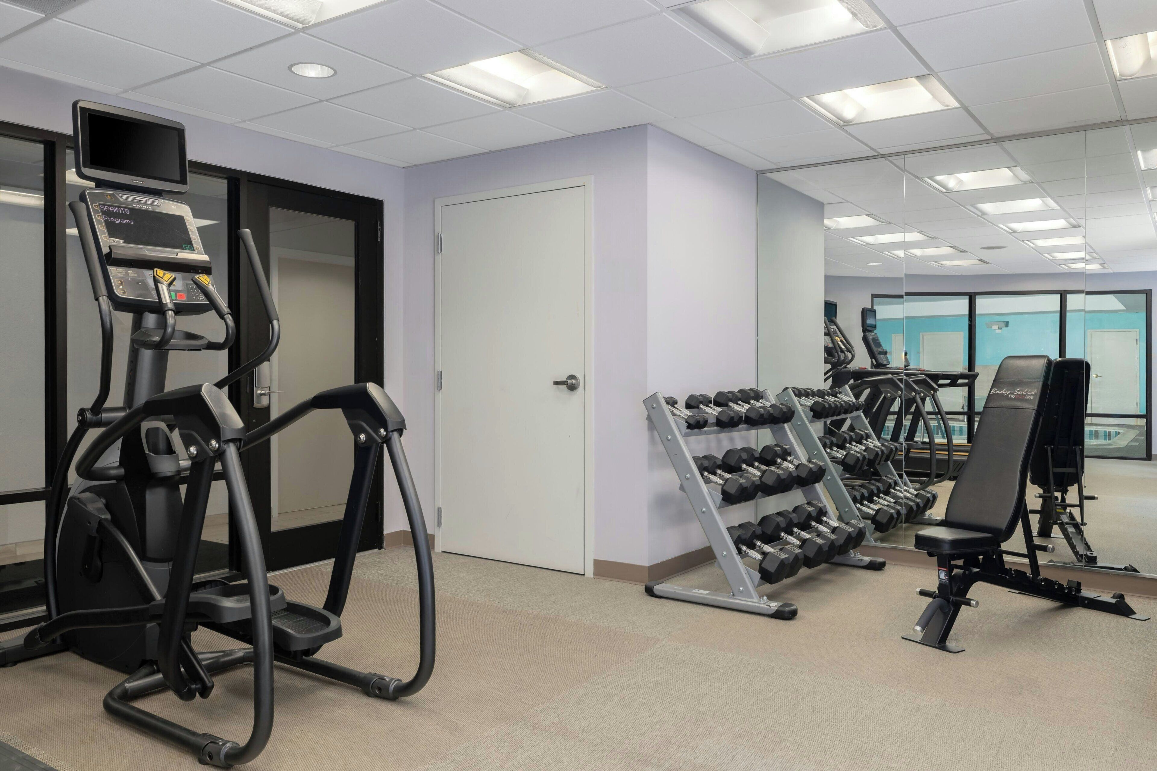 Un gimnasio con cintas de correr, una escaladora y un estante con mancuernas.