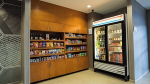Zona de venta automática con refrigerios y bebidas, que incluye un refrigerador y estantes llenos de productos.