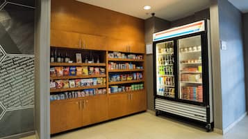 Et område med automat til snacks og drikkevarer, med et køleskab og hylder fyldt med proviant og forfriskninger.