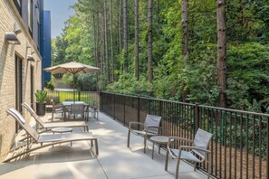 A patio with outdoor furniture, a table, and an umbrella, surrounded by a metal fence and trees.