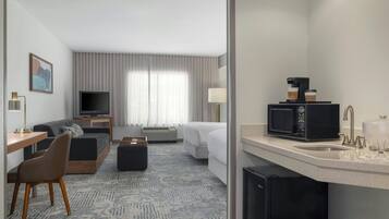 Habitación de hotel con sofá, escritorio, televisor, cafetera y kitchenette.