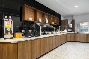 Een ontbijtruimte met zelfbediening, inclusief automaten voor wafels, een koffieapparaat en een koelkast.
