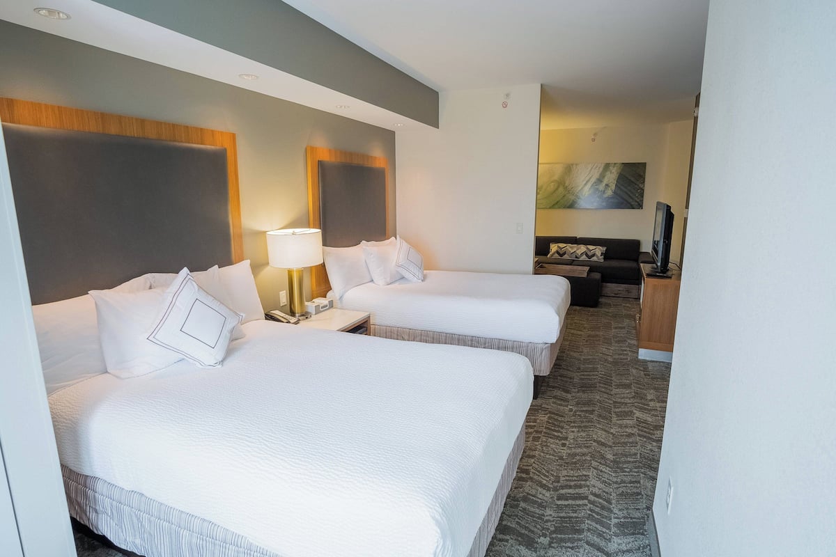 Ein Hotelzimmer mit zwei Betten, einem Fernseher, einem Schreibtisch und einem Sofa.