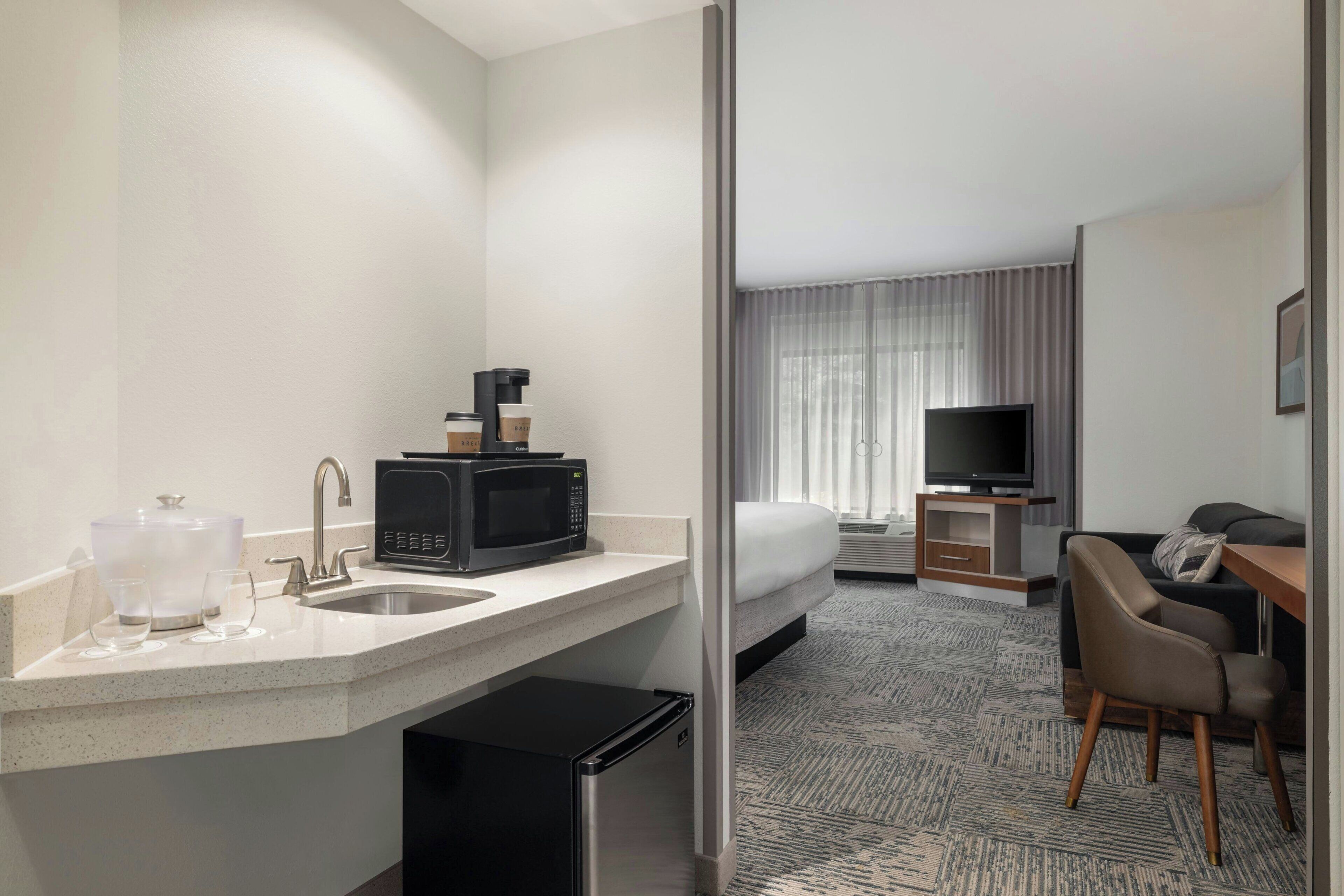 A hotel room with a kitchenette, a bed, a TV, and a seating area.