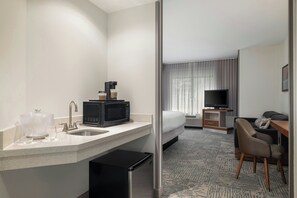 Een hotelkamer met een kitchenette, een bed, een televisie en een zithoek.