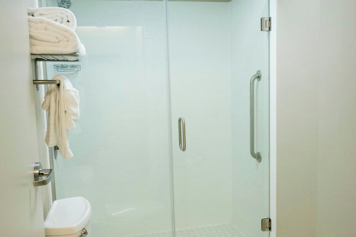 Een badkamer met toilet, een douche met glazen wand en een handdoekrek met opgevouwen handdoeken.