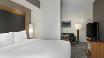 Una habitación de hotel con una cama grande, un televisor sobre un soporte de madera y un sofá con un cojín estampado.