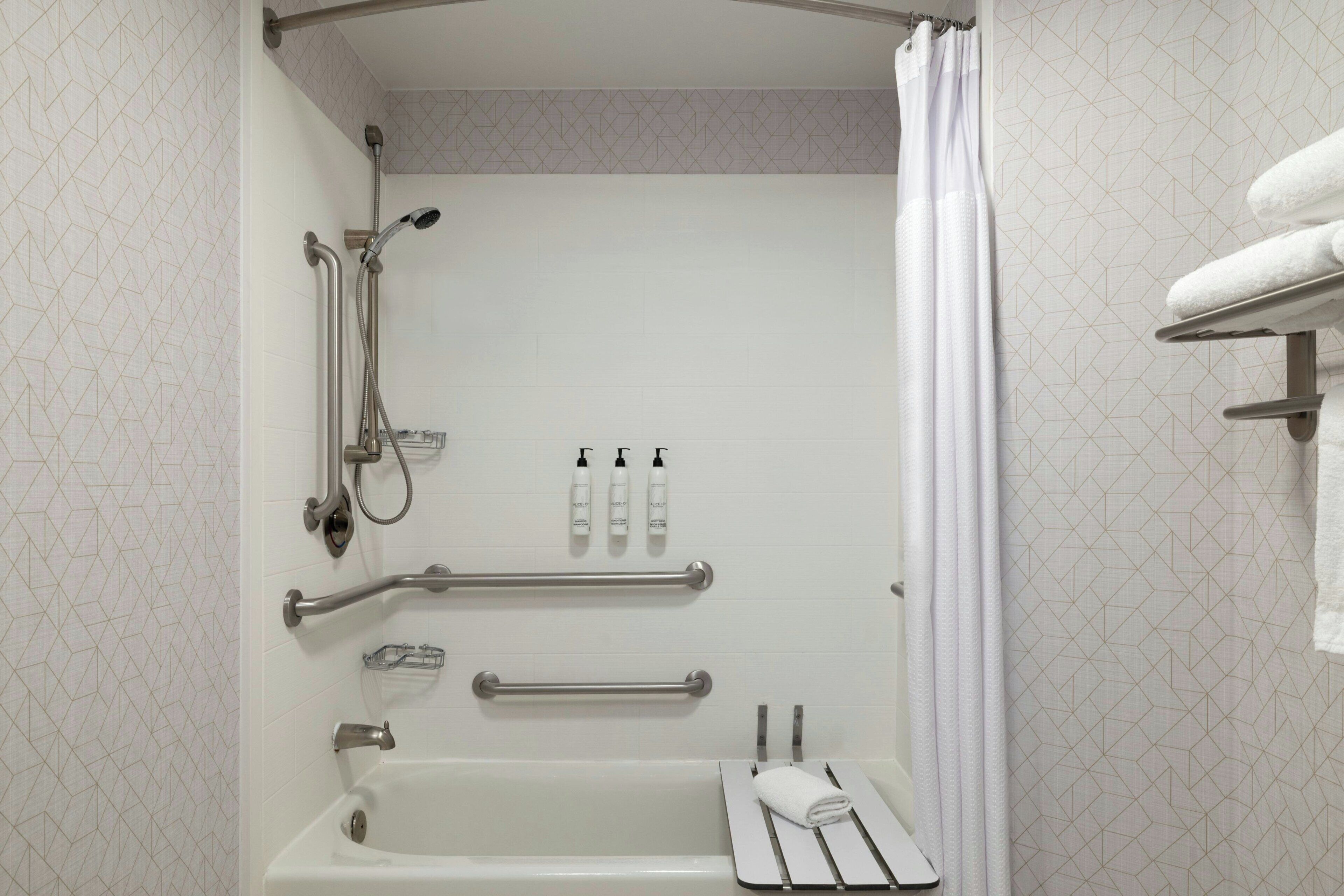 Un baño con bañera, ducha, barras de apoyo y un perchero para toallas.