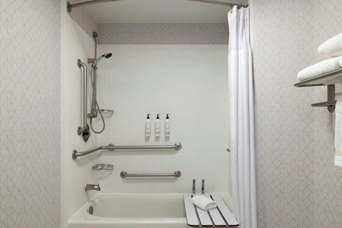 Een badkamer met een bad, douche, handgrepen en een handdoekhouder.