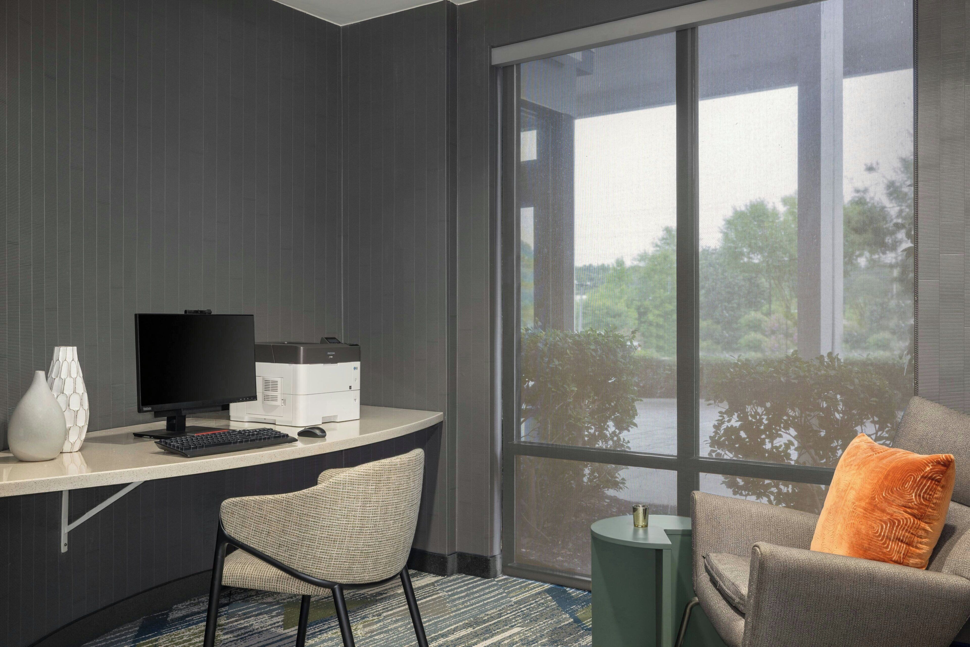 A hotel room with a desk, computer, printer, and two chairs.