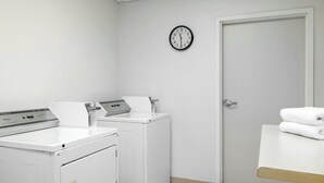 Un cuarto de lavandería con dos lavadoras, una secadora, un reloj en la pared y una puerta.