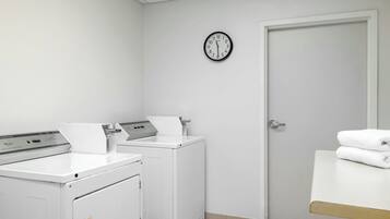A laundry room with two washing machines, a dryer, a clock on the wall, and a door.