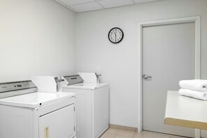 Een wasserette met twee wasmachines, een droger, een klok aan de muur en een deur.