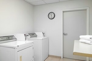 A laundry room with two washing machines, a dryer, a clock on the wall, and a door.