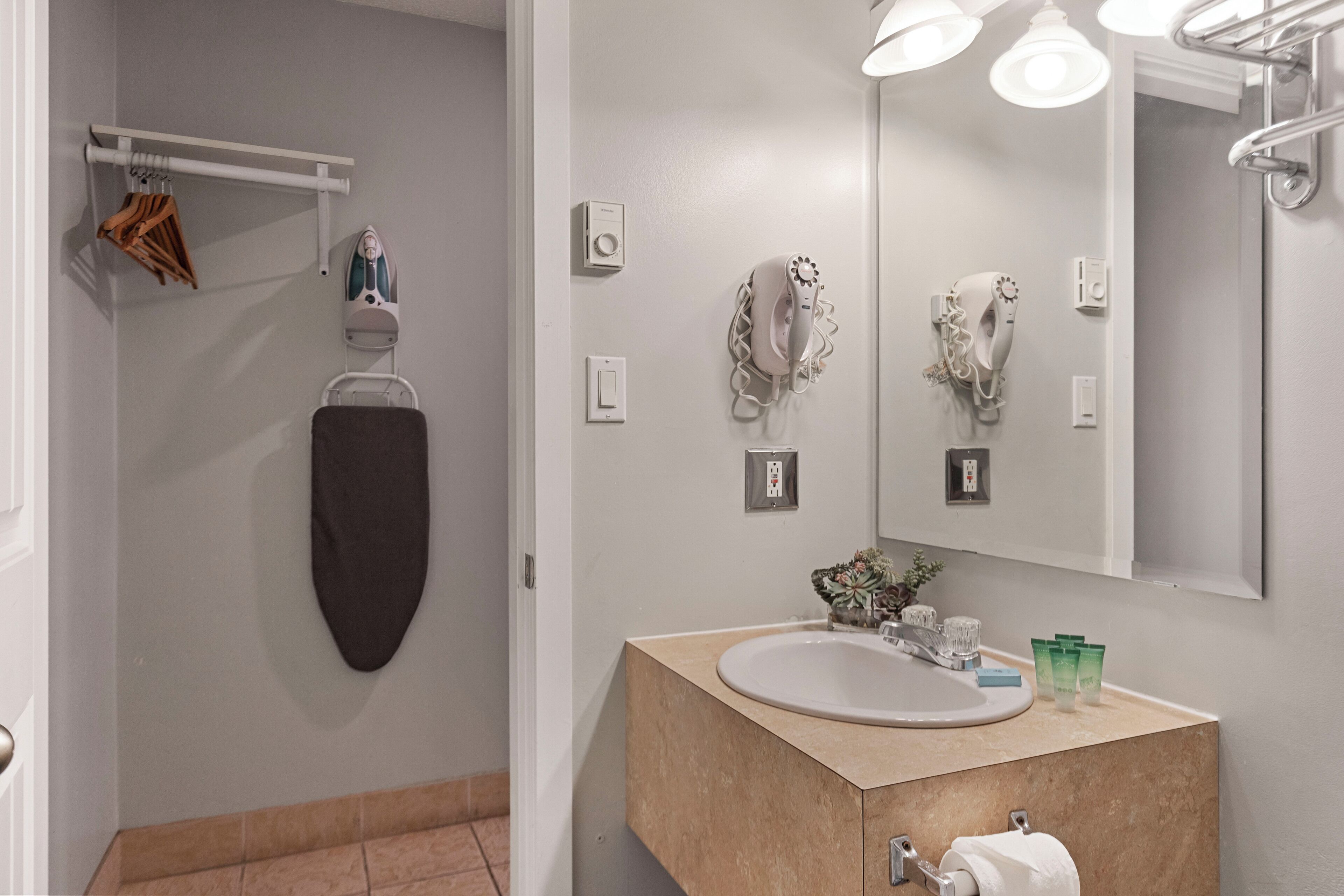 Une salle de bain avec un meuble-lavabo beige, un grand miroir, un porte-serviettes et un sèche-cheveux.