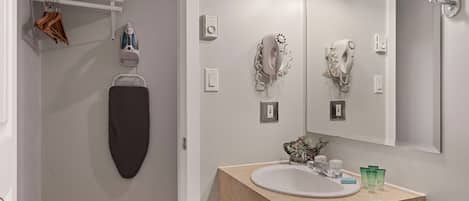 Une salle de bain avec un meuble-lavabo beige, un grand miroir, un porte-serviettes et un sèche-cheveux.