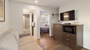 A modern, compact living space with a kitchenette, a flat-screen TV, a sofa, and a bedroom with a bed and window. - Oasis Inn (Kelowna)