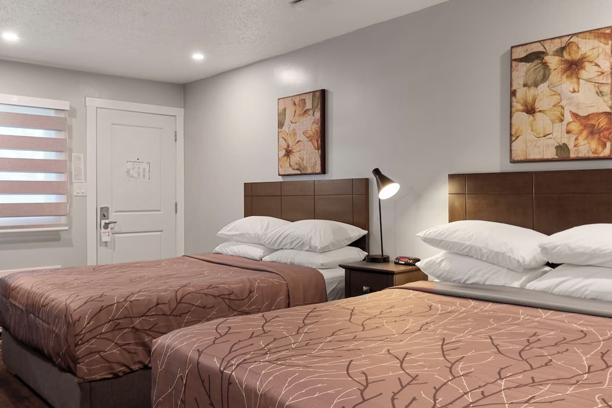 A hotel room with two beds, a wooden headboard, a nightstand with a lamp, and floral artwork on the walls.