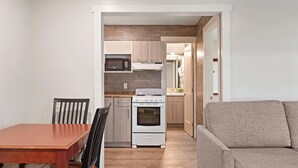 A compact kitchen with a microwave, stove, and oven, a dining table with chairs, and a sofa in a small living area. - Oasis Inn (Kelowna)