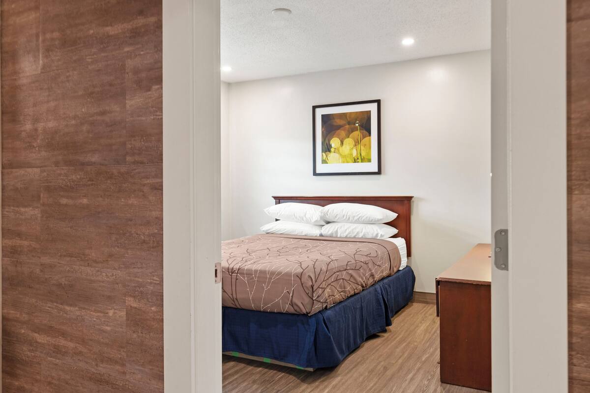 A bedroom with a bed, a bedside table, a framed picture on the wall, and a wooden floor.