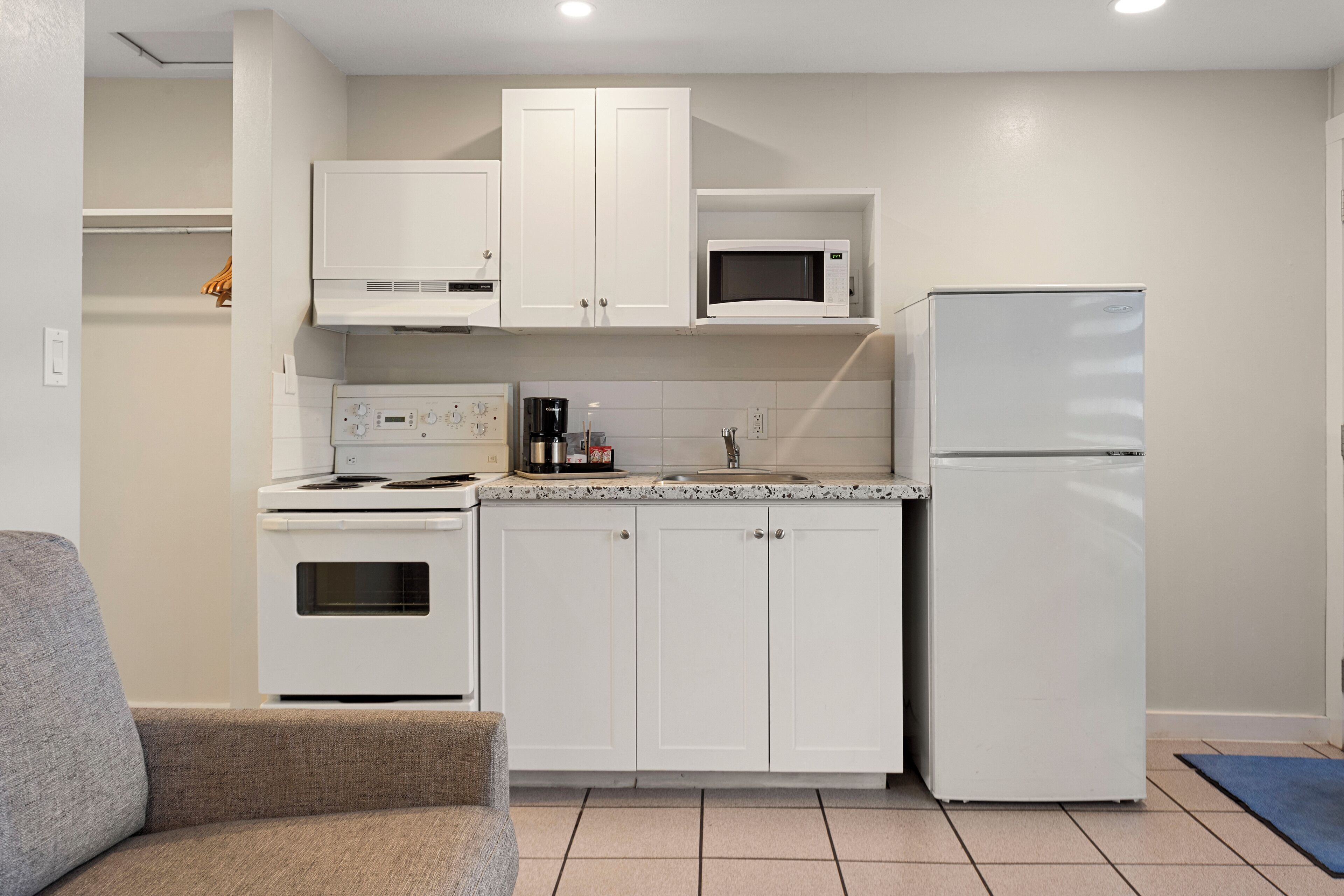 A compact kitchen with white cabinets, a microwave, a refrigerator, a stove, and a coffee maker.