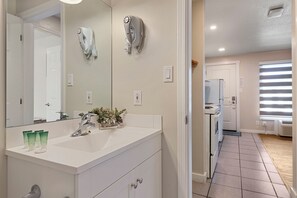 A modern bathroom with a large mirror, white vanity, and a hairdryer mounted on the wall.