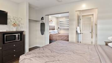 Quarto moderno com cama, guarda-roupa, micro-ondas e banheiro visível por uma porta aberta.