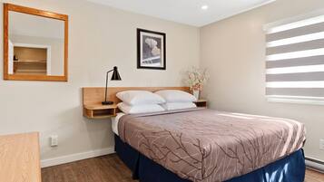 A bedroom with a bed, a nightstand, a mirror, a framed picture, and a window with blinds.