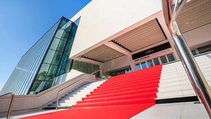 A modern building with a glass facade and a red staircase leading to a white entrance. - Hôtel Cannes Croisette (Cannes)