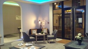 A modern hotel lobby with a seating area, a table set for dining, and a view of the street outside. - Hôtel Cannes Croisette (Cannes)