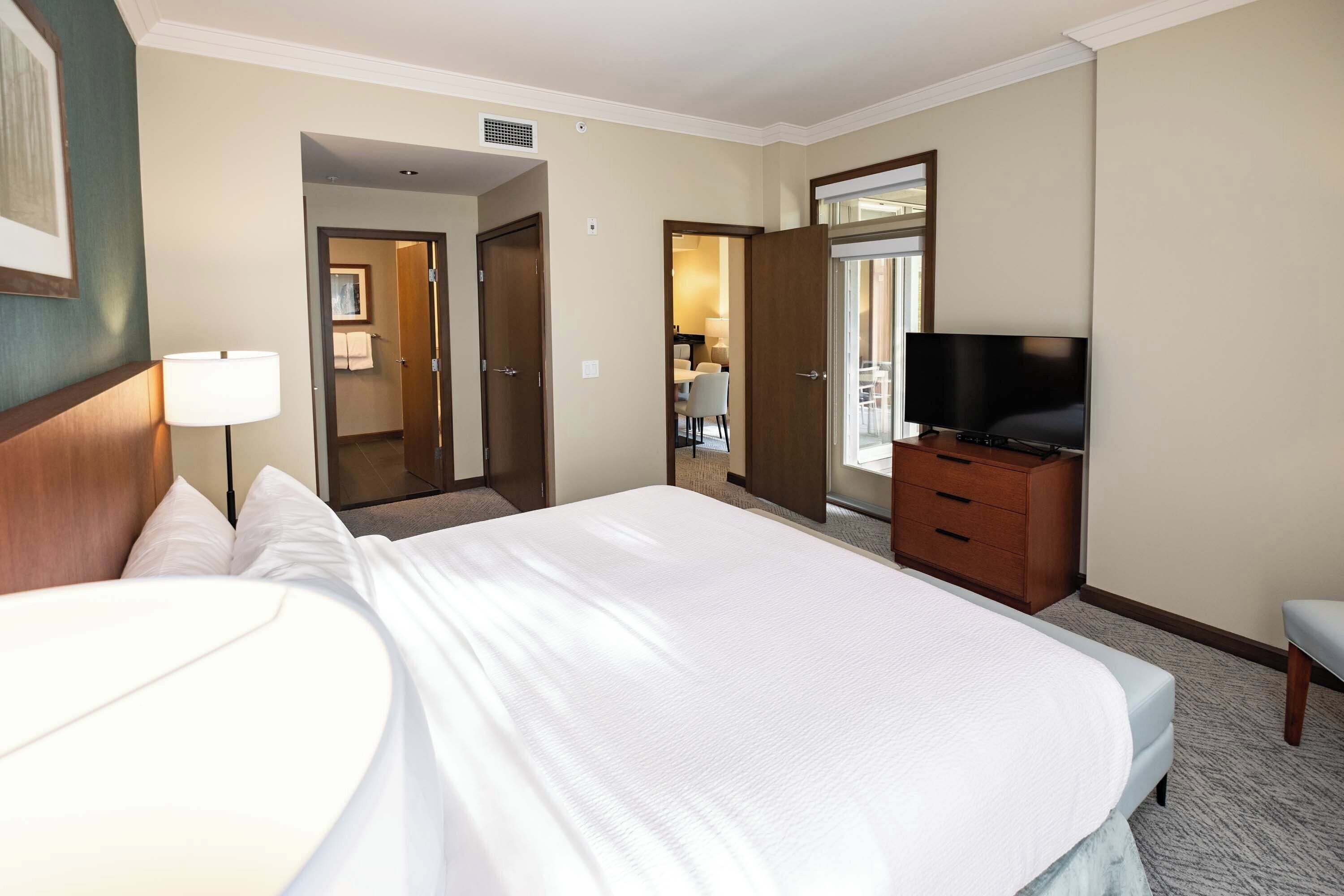 A hotel room with a large bed, a television, a dresser, and a desk.