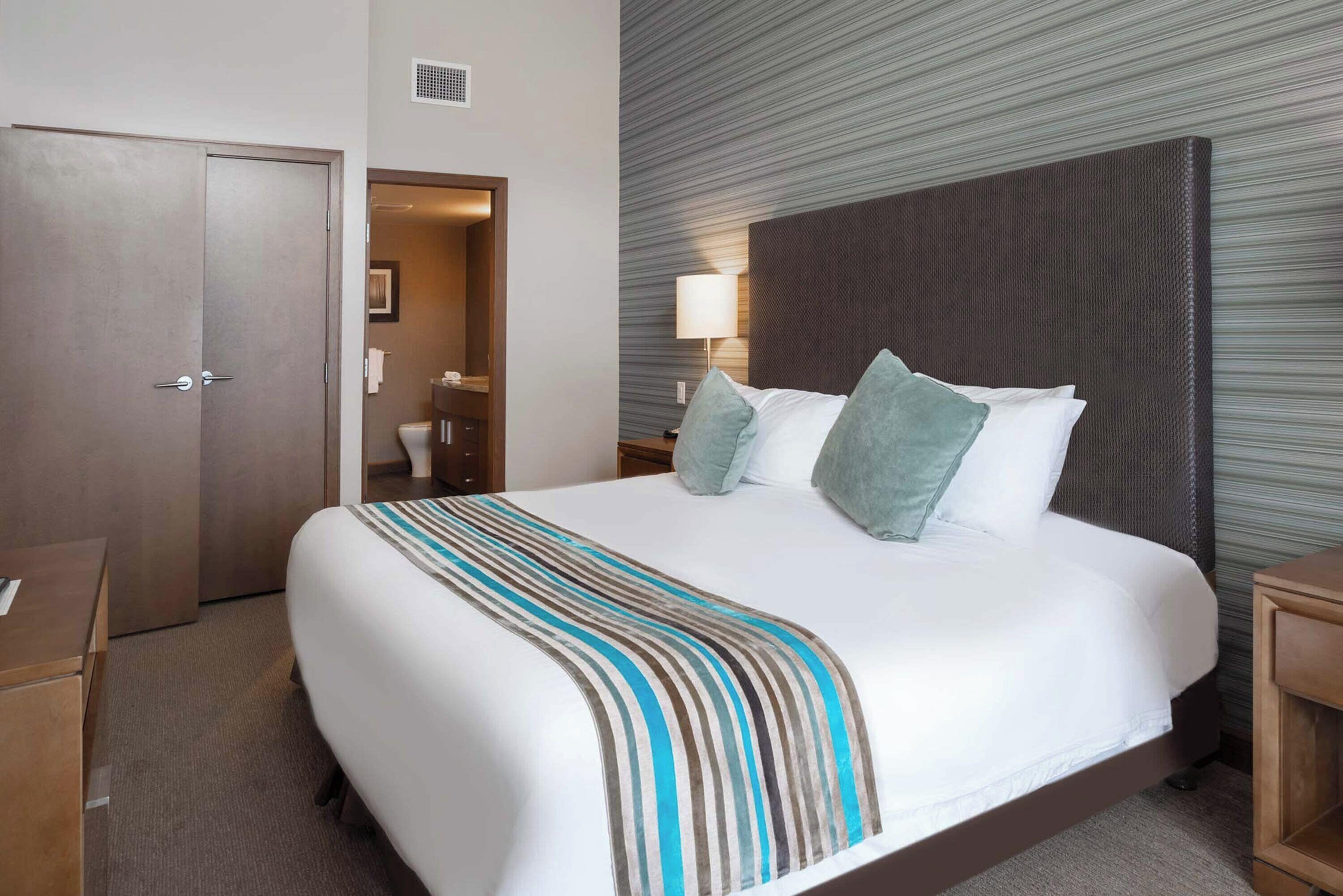 A hotel room with a large bed, a wooden nightstand, a desk, and a door.