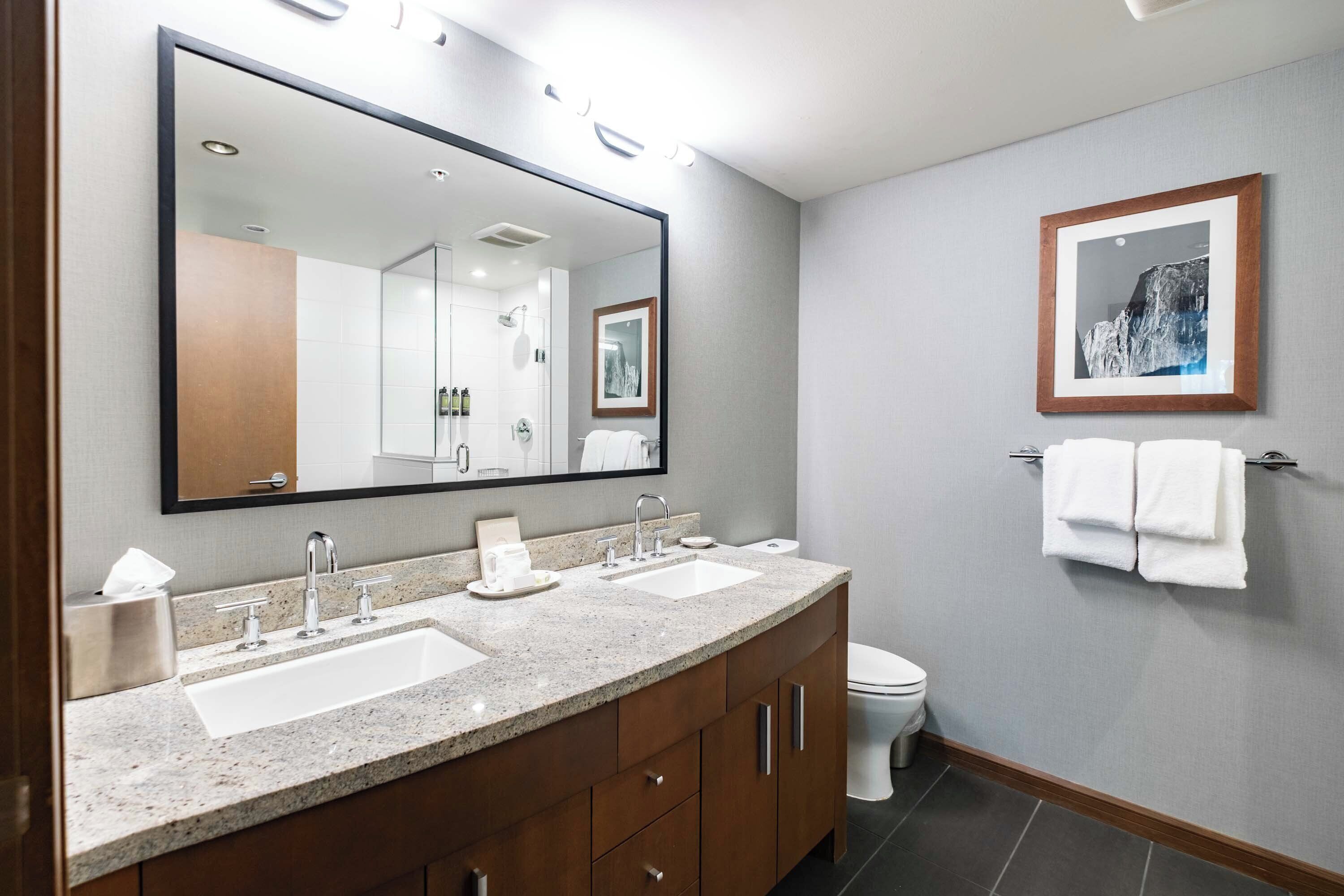 A modern bathroom with a large mirror, two sinks, a toilet, and a framed picture on the wall.