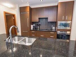A modern kitchen with granite countertops, stainless steel appliances, and brown cabinetry.
