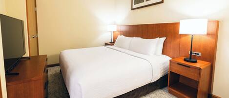 A hotel room with a large bed, two bedside tables with lamps, a TV on a wooden cabinet, and a framed picture on the wall.