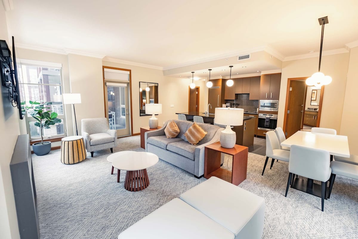 Een moderne woonkamer met een grijze bank, een witte salontafel en een eethoek met witte stoelen.