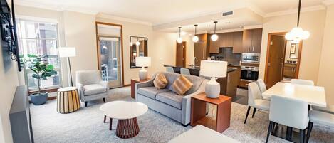 A modern living room with a grey sofa, white coffee table, and dining area with white chairs.