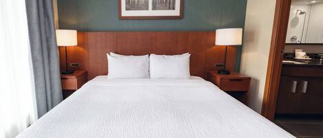 A hotel room with a large bed, two bedside tables with lamps, a framed picture on the wall, and a view into the bathroom.